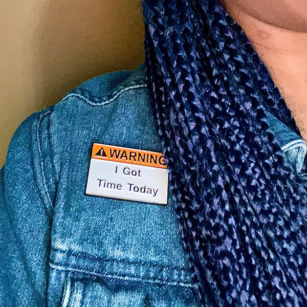 Warning! I Got Time Today enamel pin in traditional orange and white hazard-themed colors on a denim jacket. Black lettering: Warning has orange background, I Got Time Today has white background.
