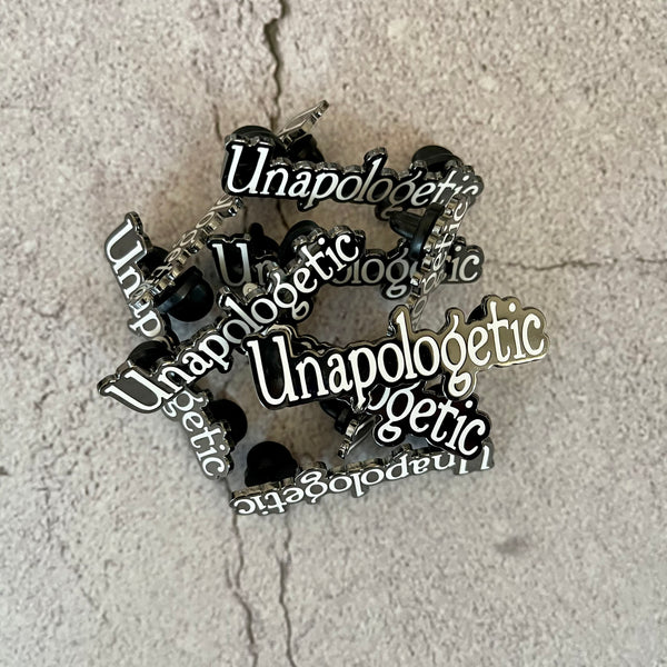 Pile of white Unapologetic word enamel pins.