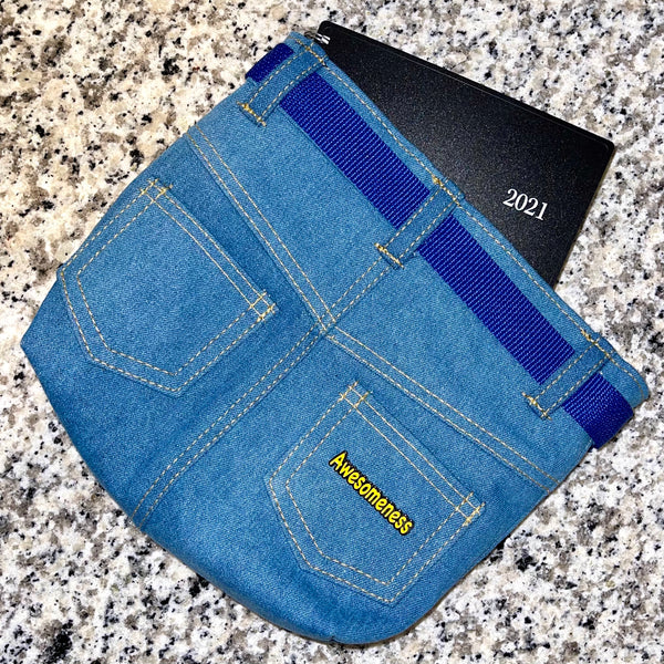 Yellow Awesomeness enamel pin on a blue denim pouch with a planner sticking out of the pouch.