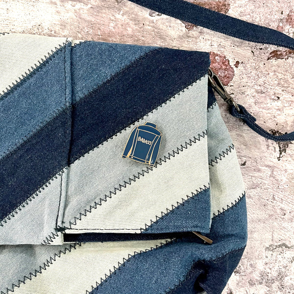 Badass Denim Jacket enamel pin on a blue denim clutch purse.