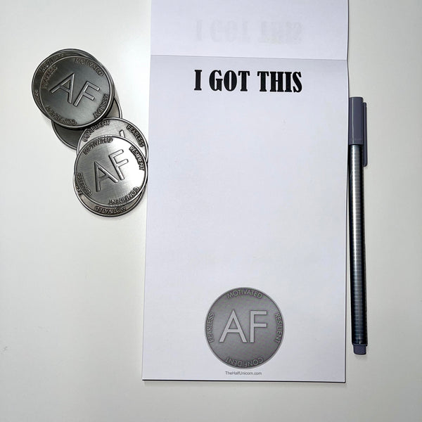 Notepad with I Got This at top and image of our silver As F**k Token at the bottom. Stack of these silver tokens and a gray pen sitting as props beside notepad.