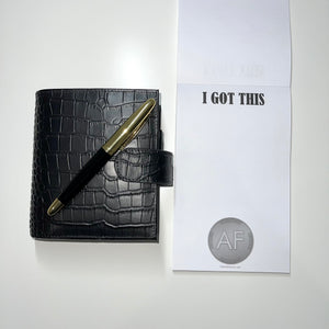I Got This notepad. Image of silver As F**k Token on bottom. Black croc planner with pen prop sitting beside notepad.
