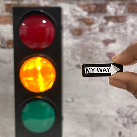 My Way Sign Enamel Pin. It has  One Way Sign vibes and is being held beside a traffic light. The yellow light is lit up.