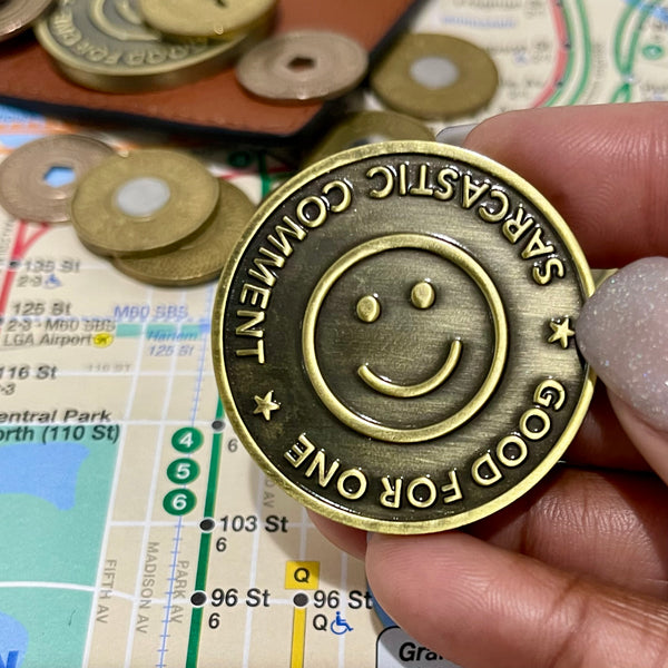 Good For One Sarcastic Comment token in a burnished gold color designed to look like an old subway token. Upside down smile in center of token. 