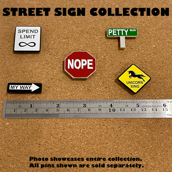 Five different humorous street sign enamel pins on a cork board - Spend Limit is like Speed Limit, Nope is like a Stop Sign, Petty Blvd is like a street sign, My Way is like a One Way sign, and Unicorn Crossing is like Deer XING.