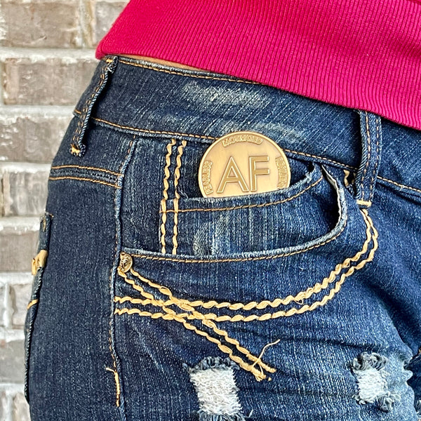 As F**k Token in worn gold color sits in the small pocket of denim shorts.